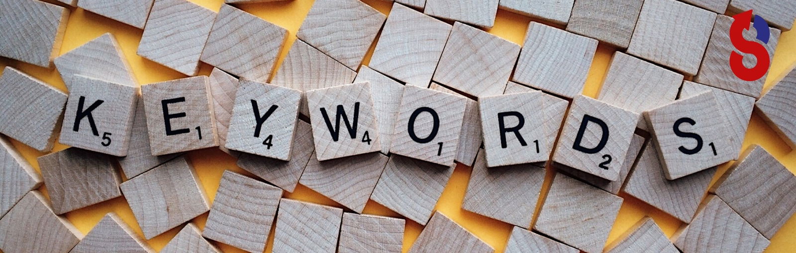 Scrabble-Buchstaben, die das Wort 'KEYWORDS' auf einem gelben Hintergrund bilden, mit einem leuchtend roten und blauen Google 'G'-Symbol in der oberen rechten Ecke, symbolisieren die Keyword-Recherche für SEO.
